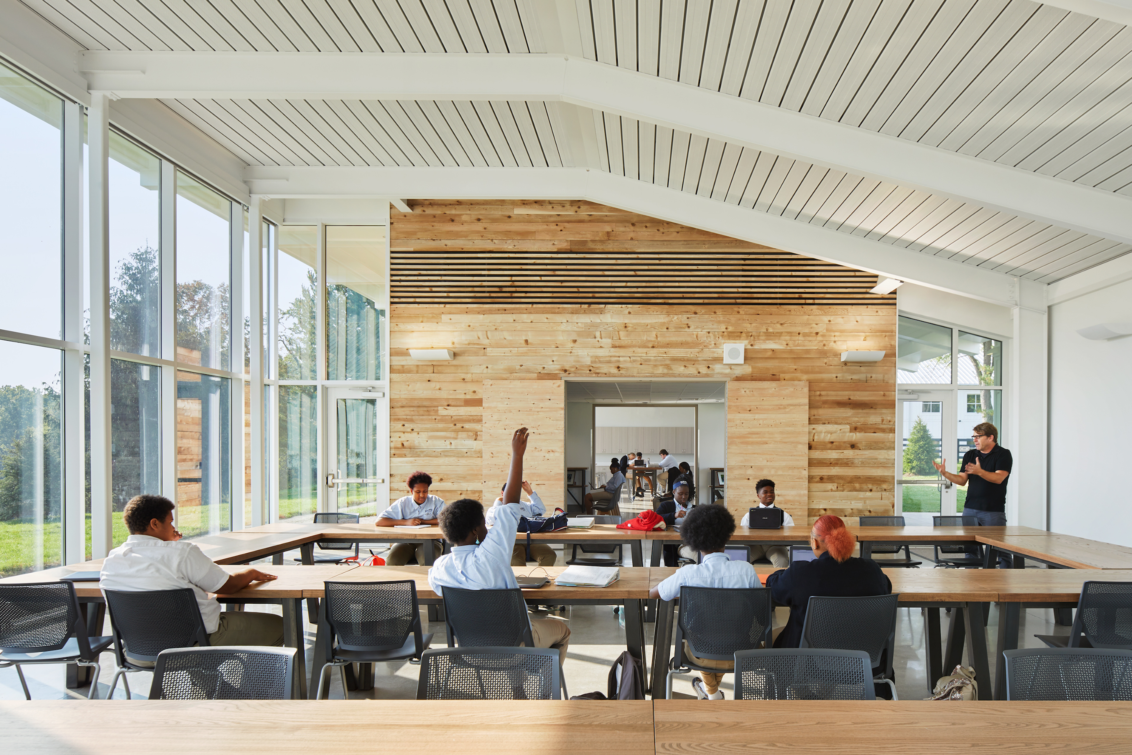 Students sat around tables in large square formation with large windows looking out to field on the left