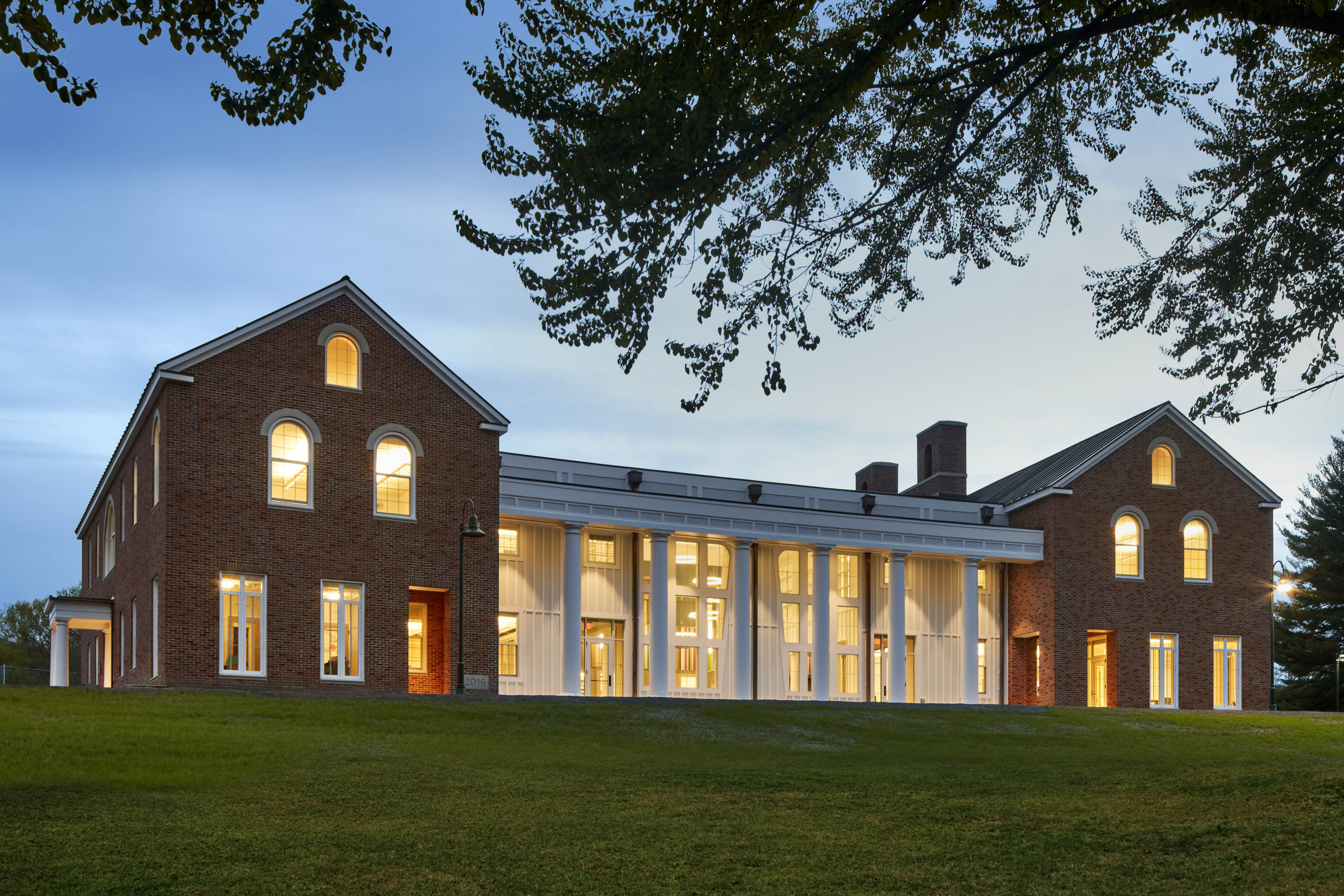 View of entrance from grassy area with brick buildings on left and right side and white building area in center