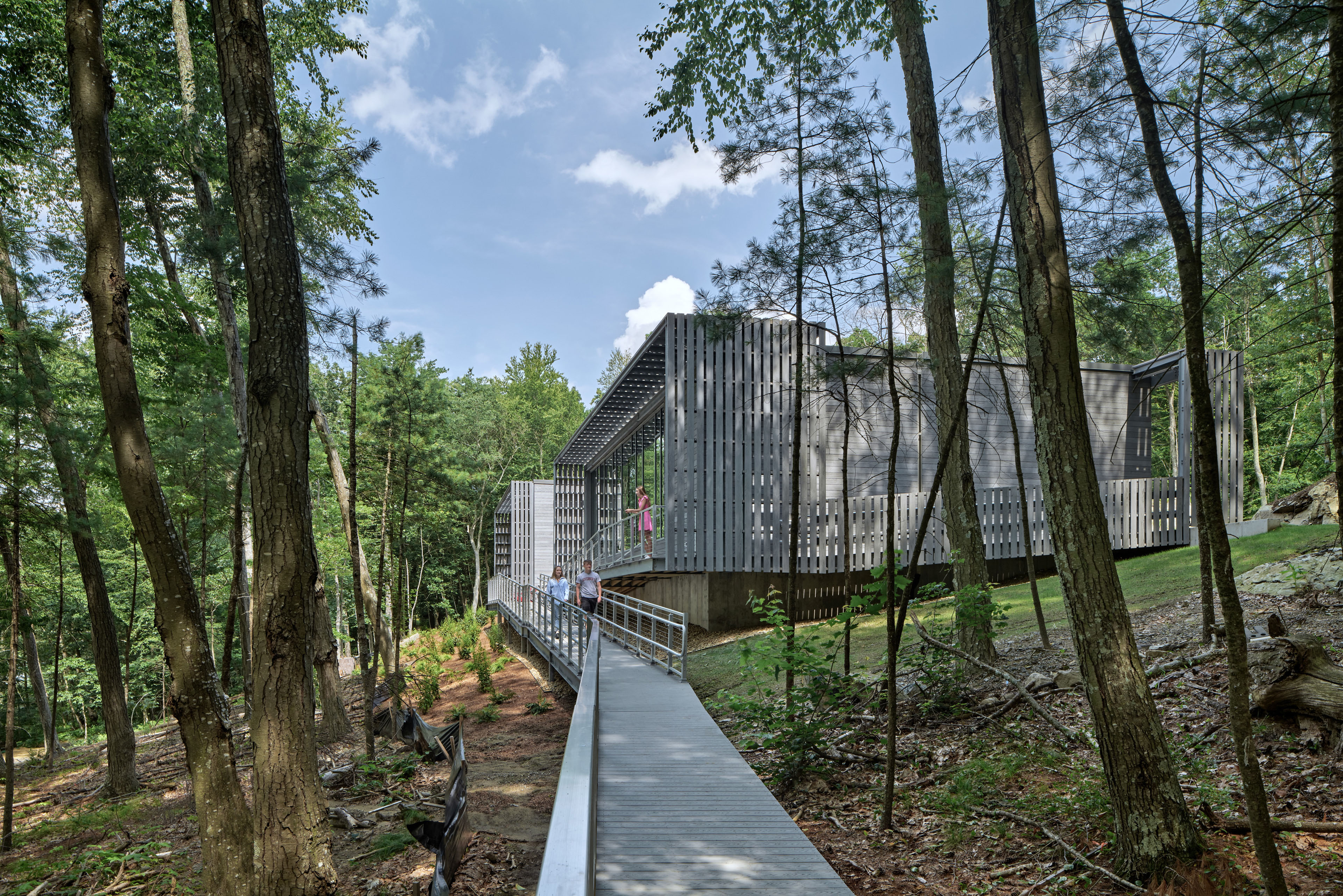 Exterior of Bill ’67 and Peter ’71 Alfond Coastal Research Center at Governor’s Academy in Byfield, MA, long ADA compliant ramp leading to back of building, surrounded by lush green forrest and blue sky.