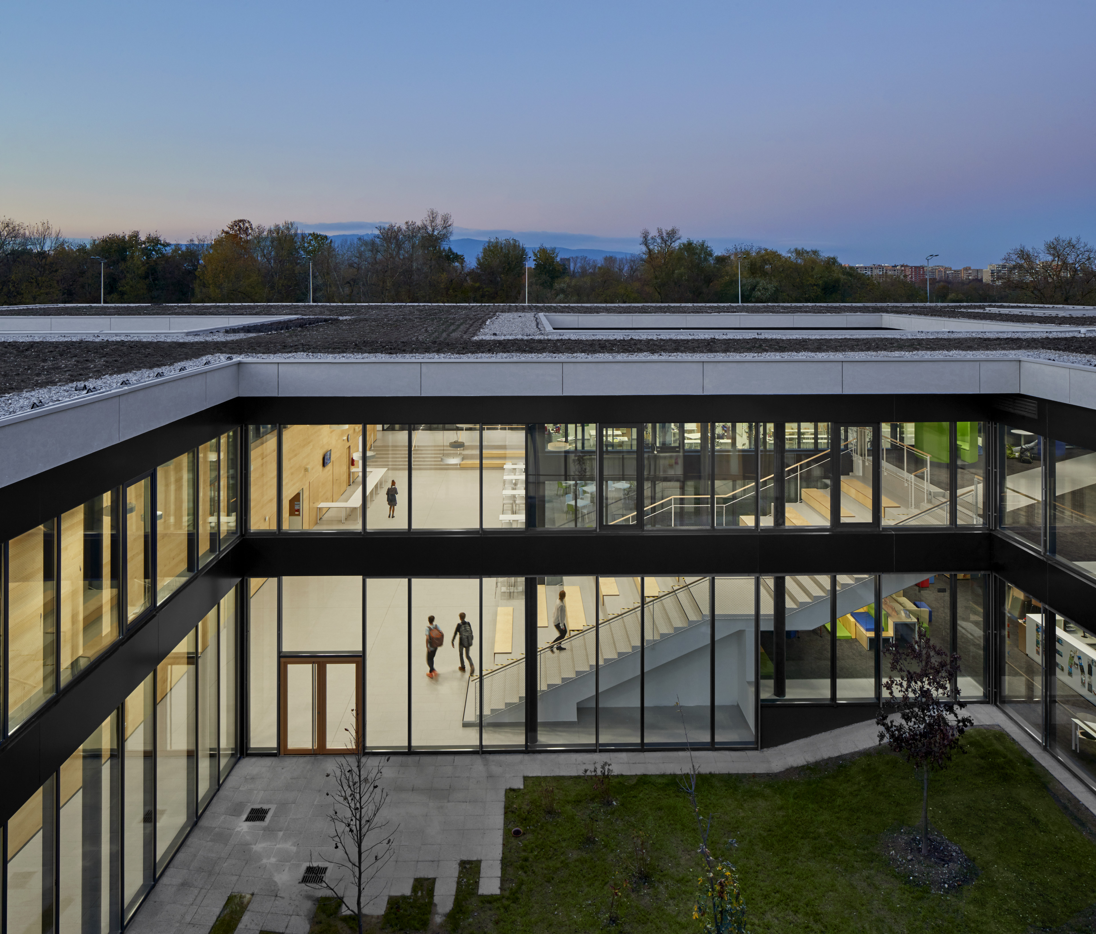 Aerial view of courtyard of American International School of Zagreb at dusk with large staircase and vertical windows surrounding 