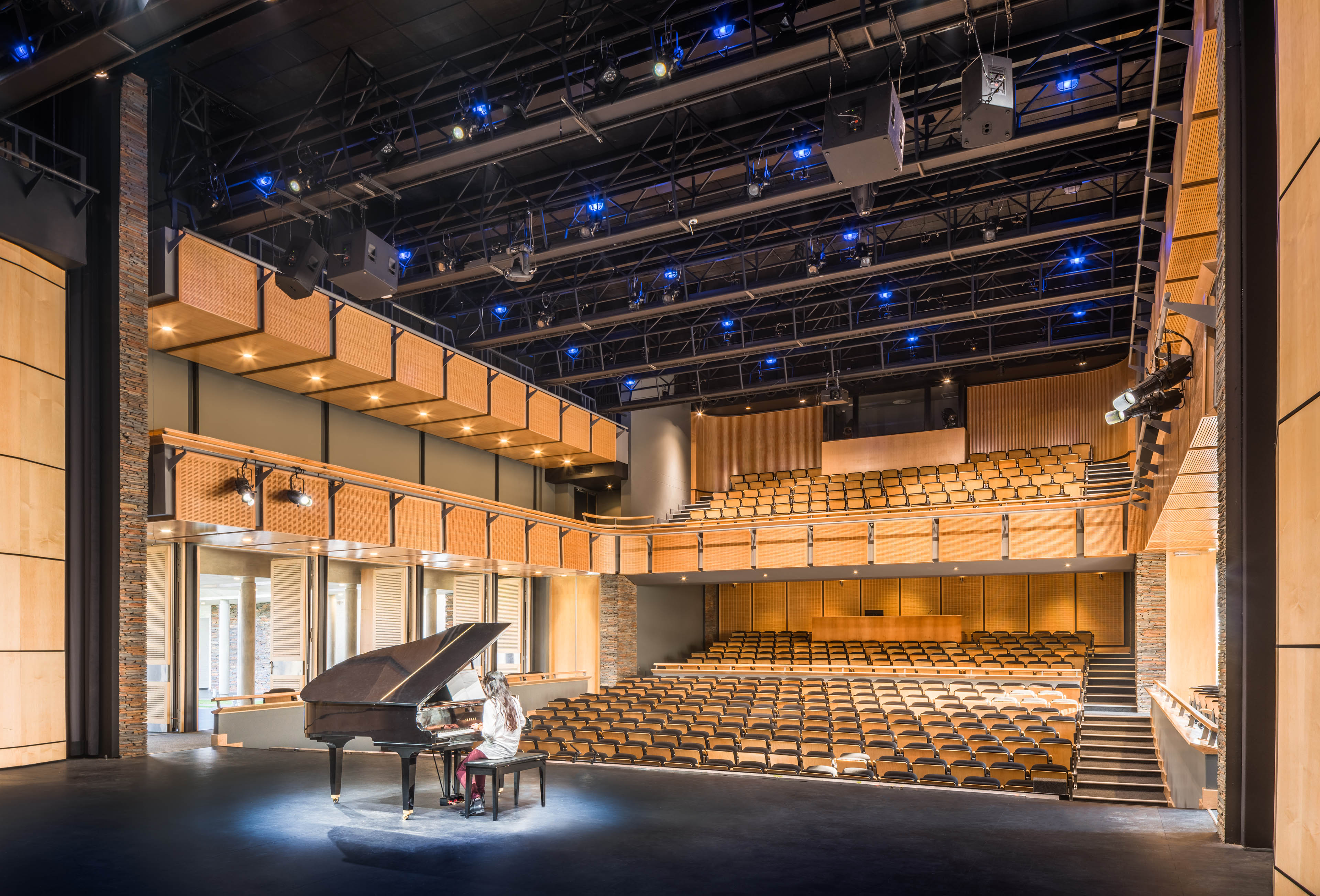 Theater from back of stage, girl sitting at grand piano with spotlight looking out at empty seats with lights on