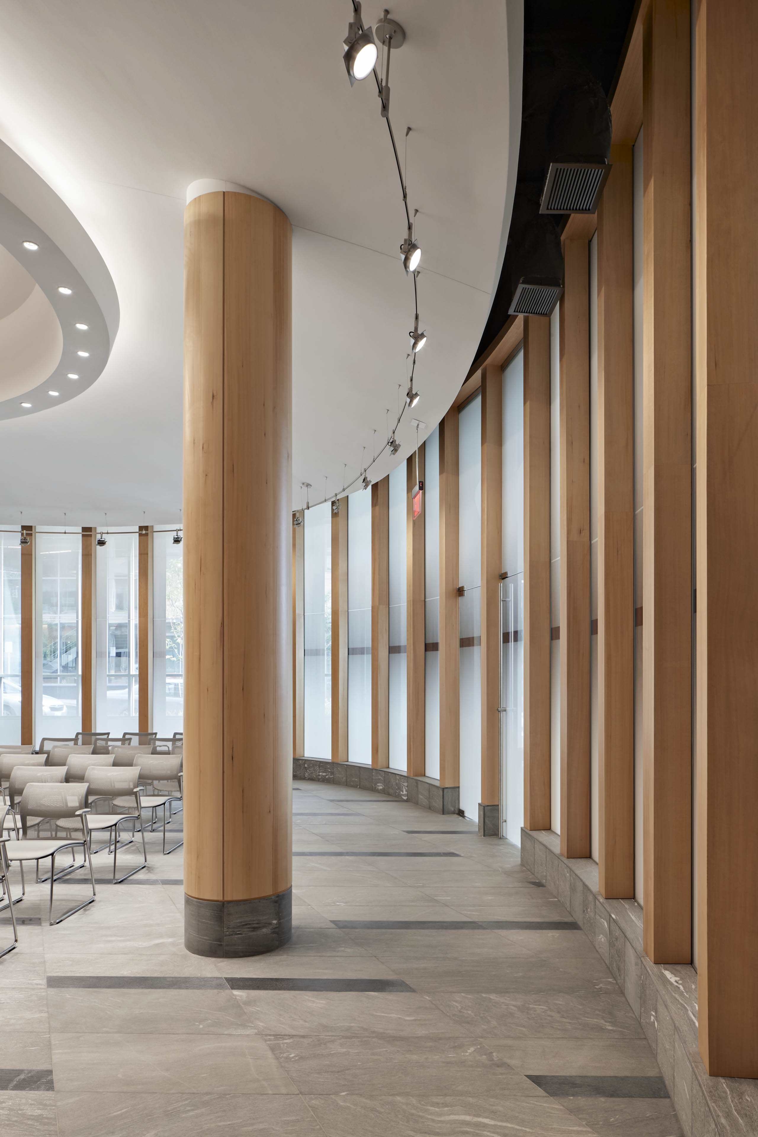 Meeting room with large wood pole and alternating wood and tall vertical windows curving around wall with bright lights