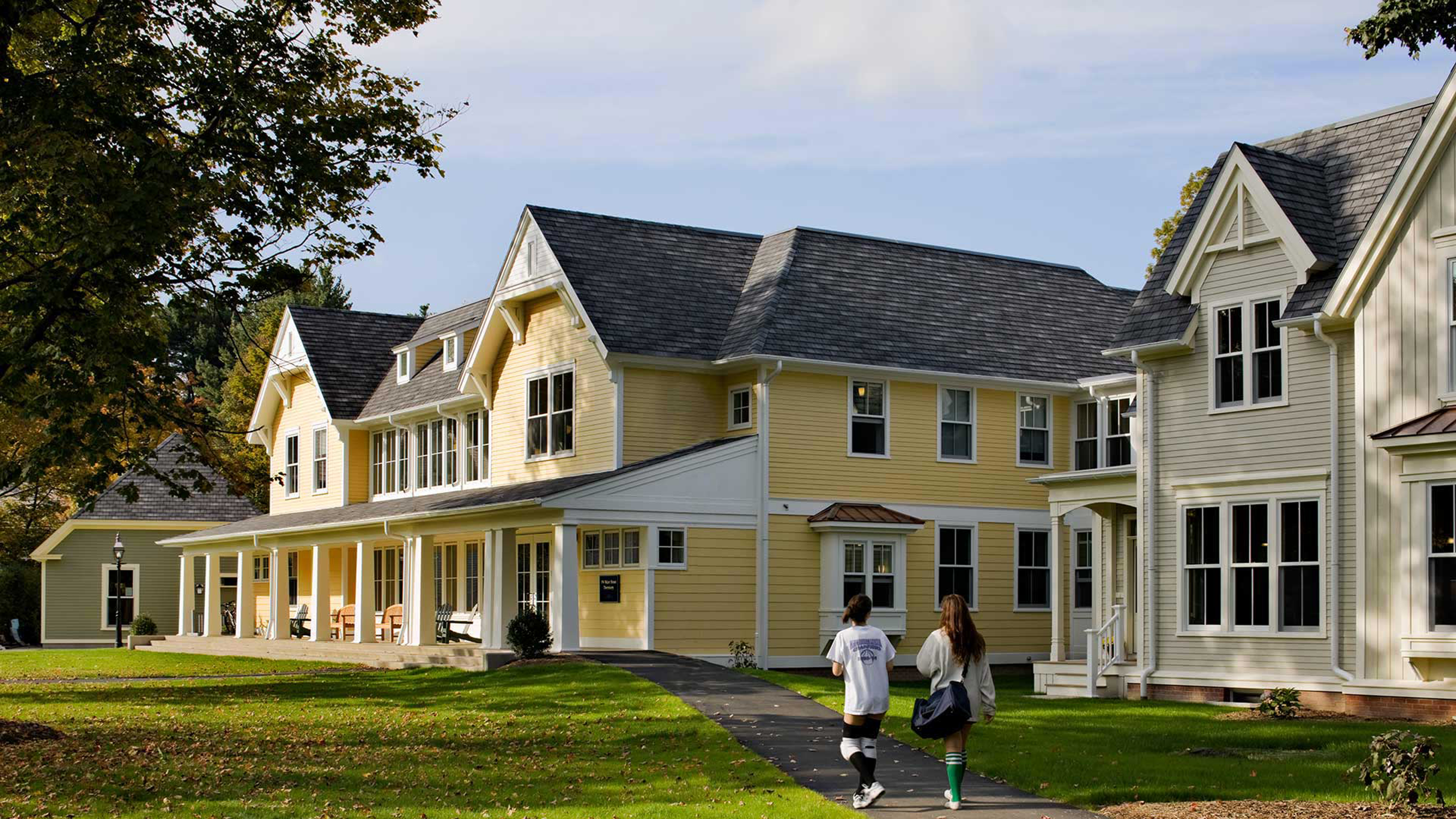 Students walking by exterior of building with yellow paint and white accents 