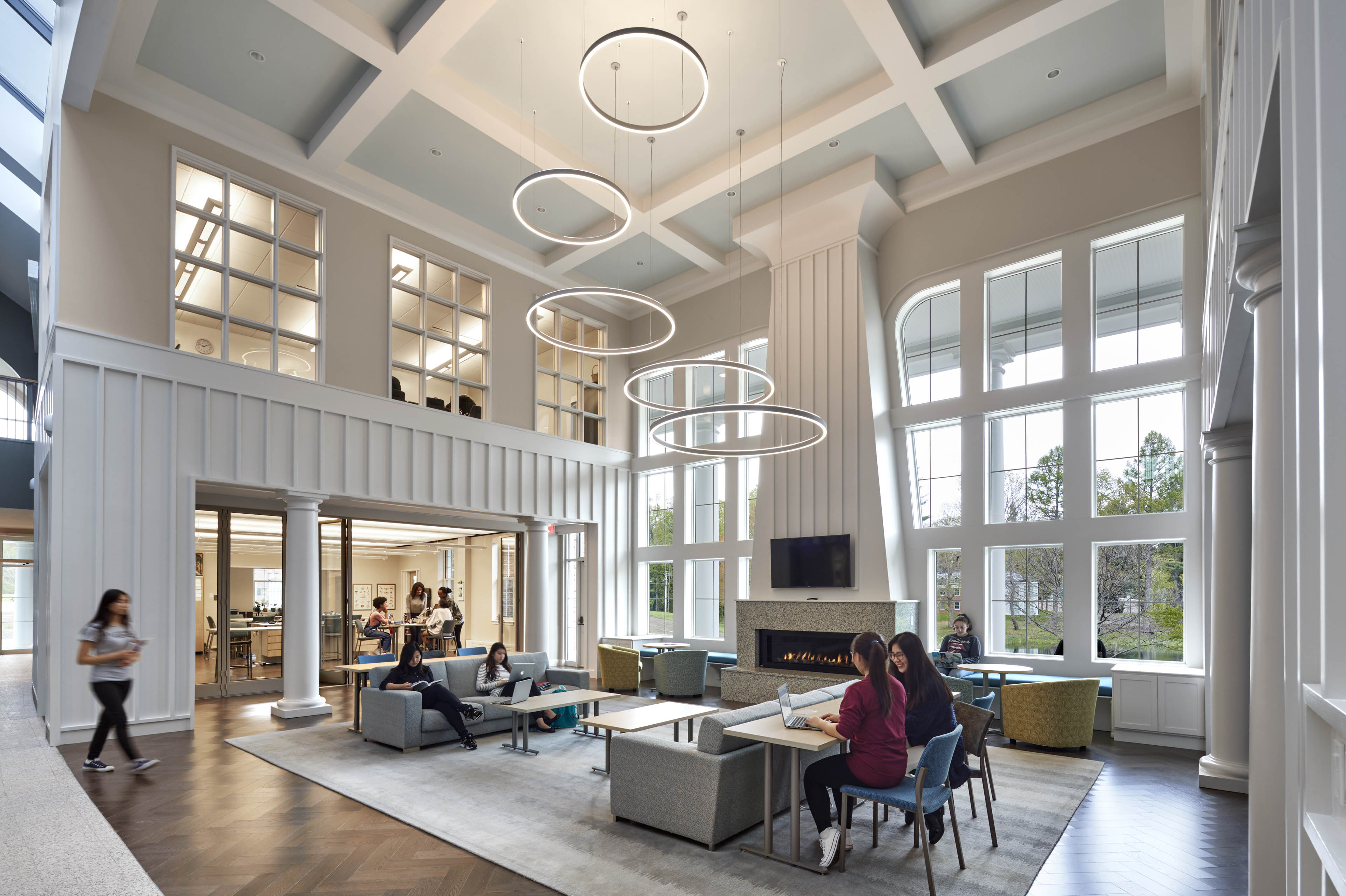 Students sat at lounge area with circular lights above and natural light coming in from windows on all sides
