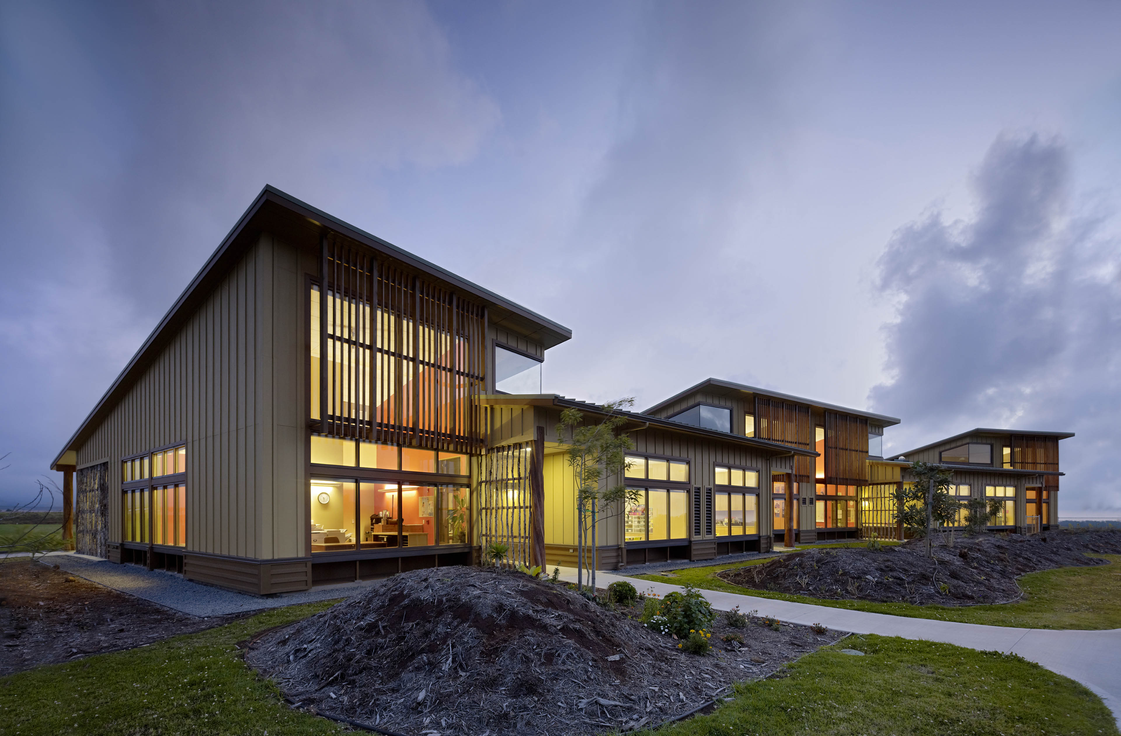 Exterior view of building at dusk with yellow and orange light peaking through windows