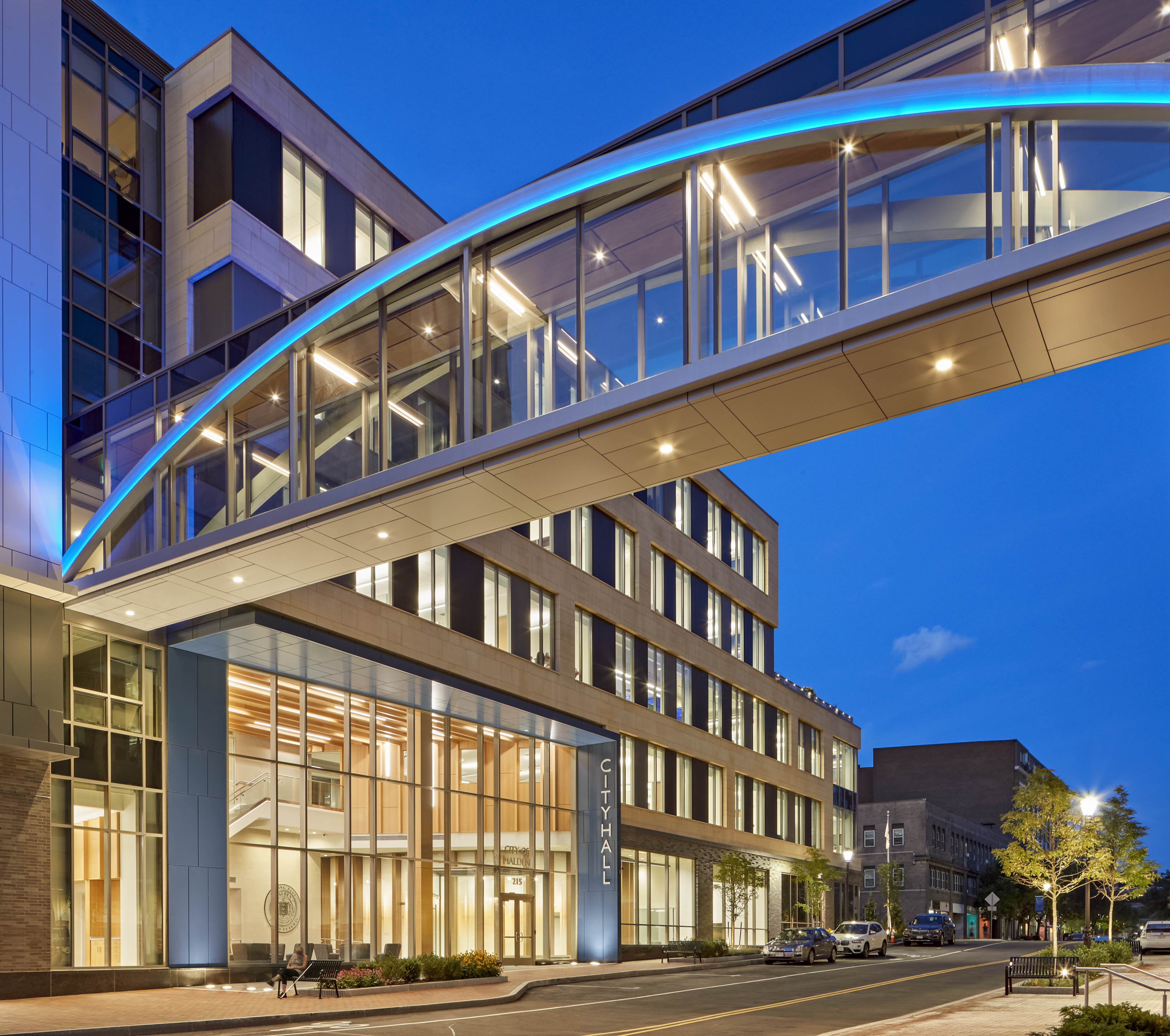 View from street at night. Entrance seen with skybridge walkway above and blue sky behind