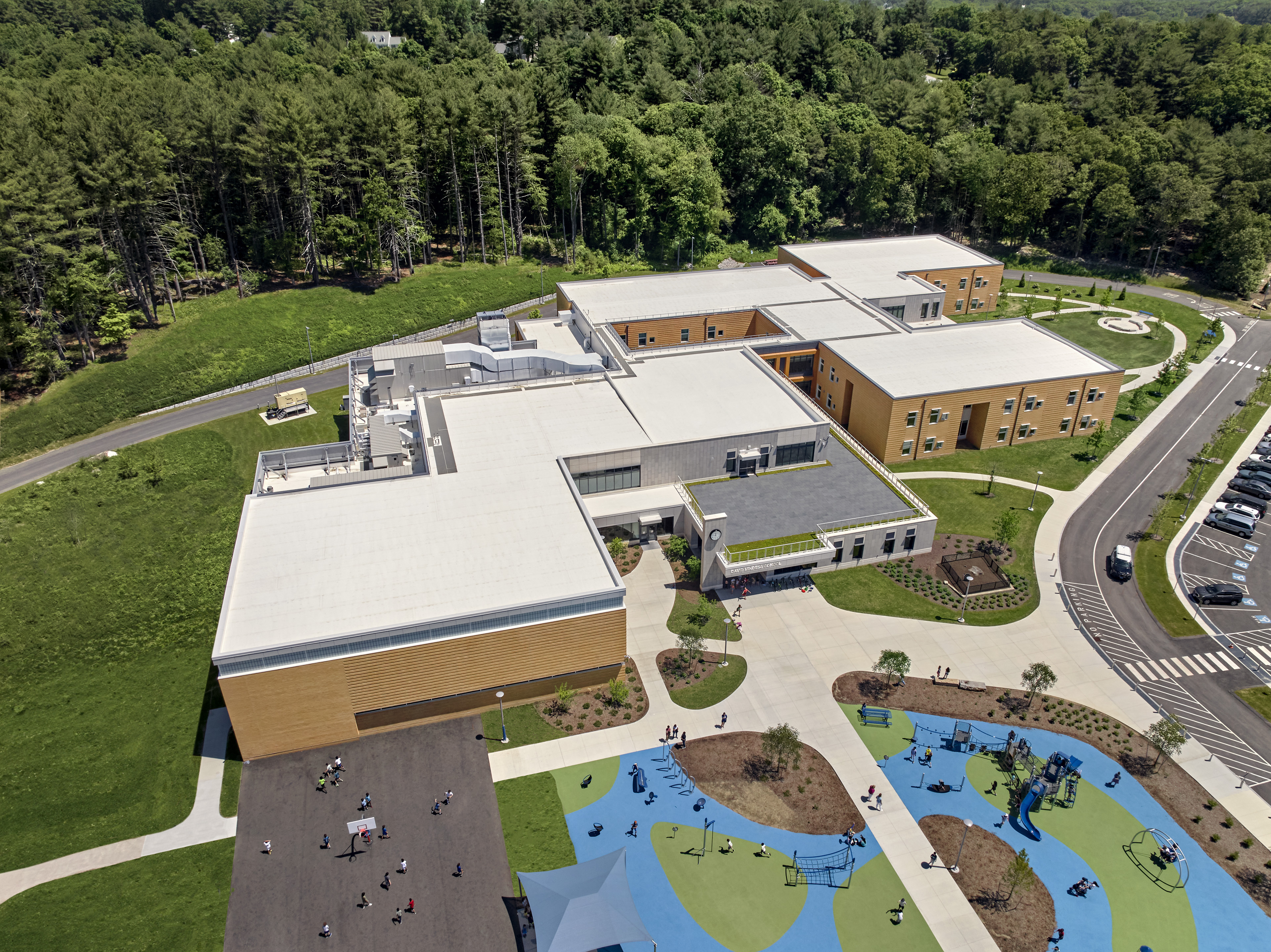 Aerial view of school with trees lining the back, playground in front and drop off lane to the right