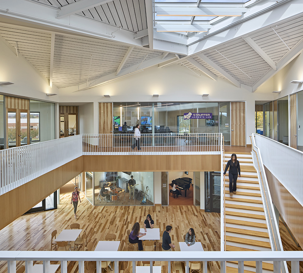 Interior staircase with students seated at tables below, white ceilings and light brown wood