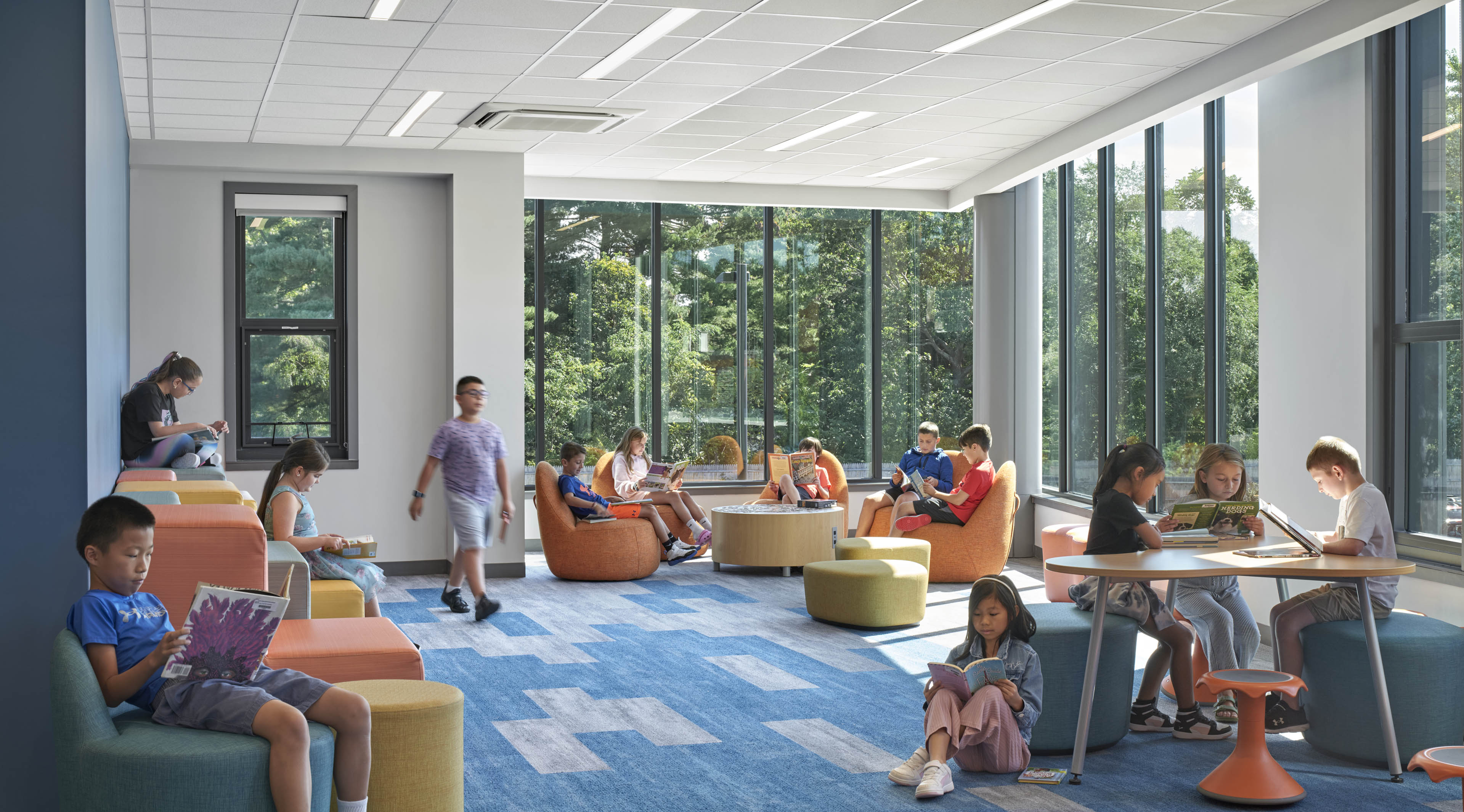 Students reading on modular lounge chairs with windows on back and right side looking out to greenery