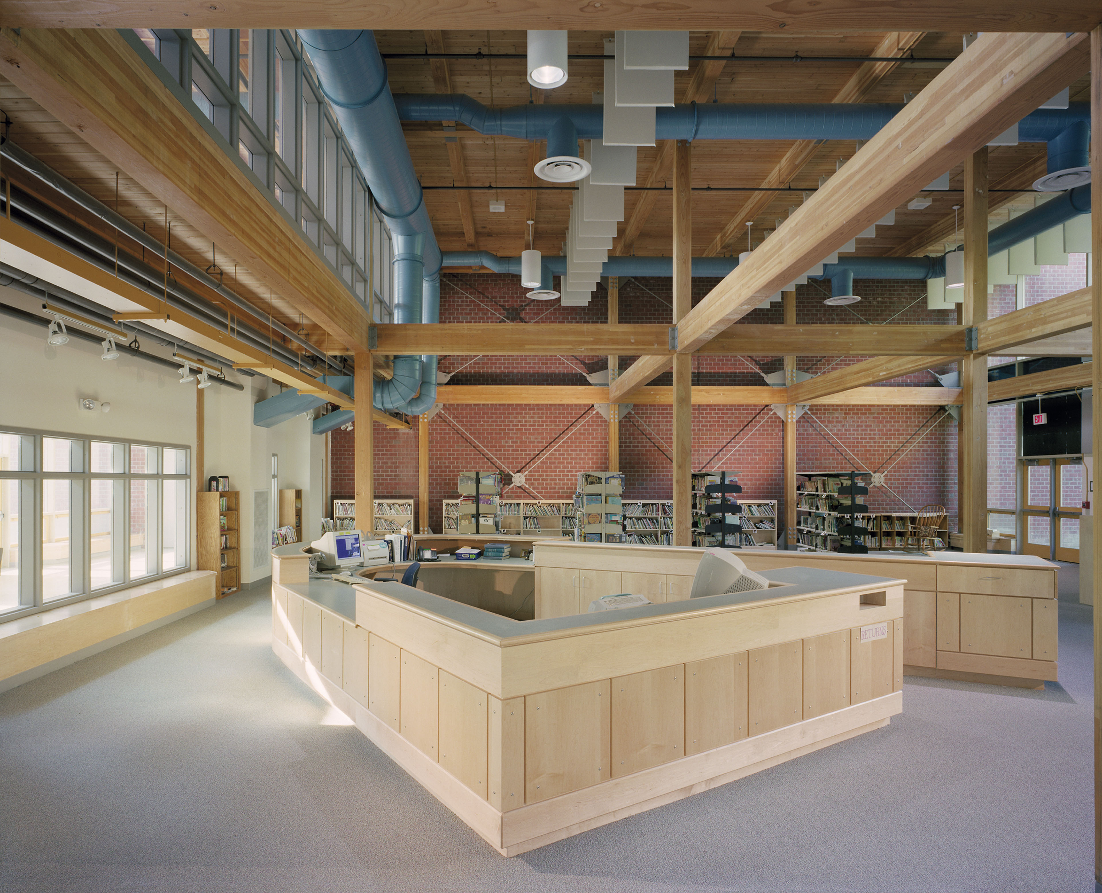 Library in center with shelving carts along back wall. Wood beams and paneling on ceiling