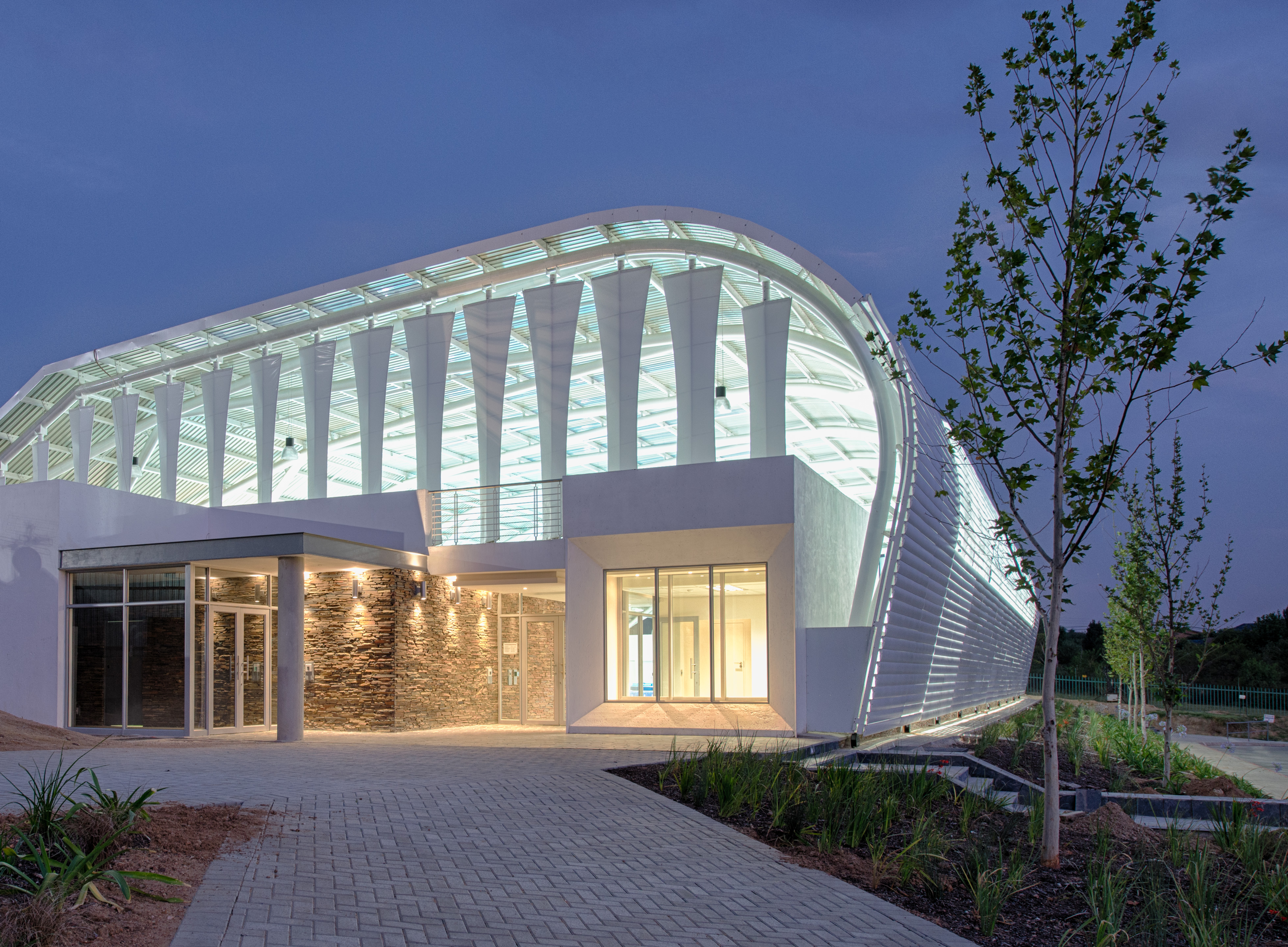 Exterior of pool building at dusk with foliage to the right side