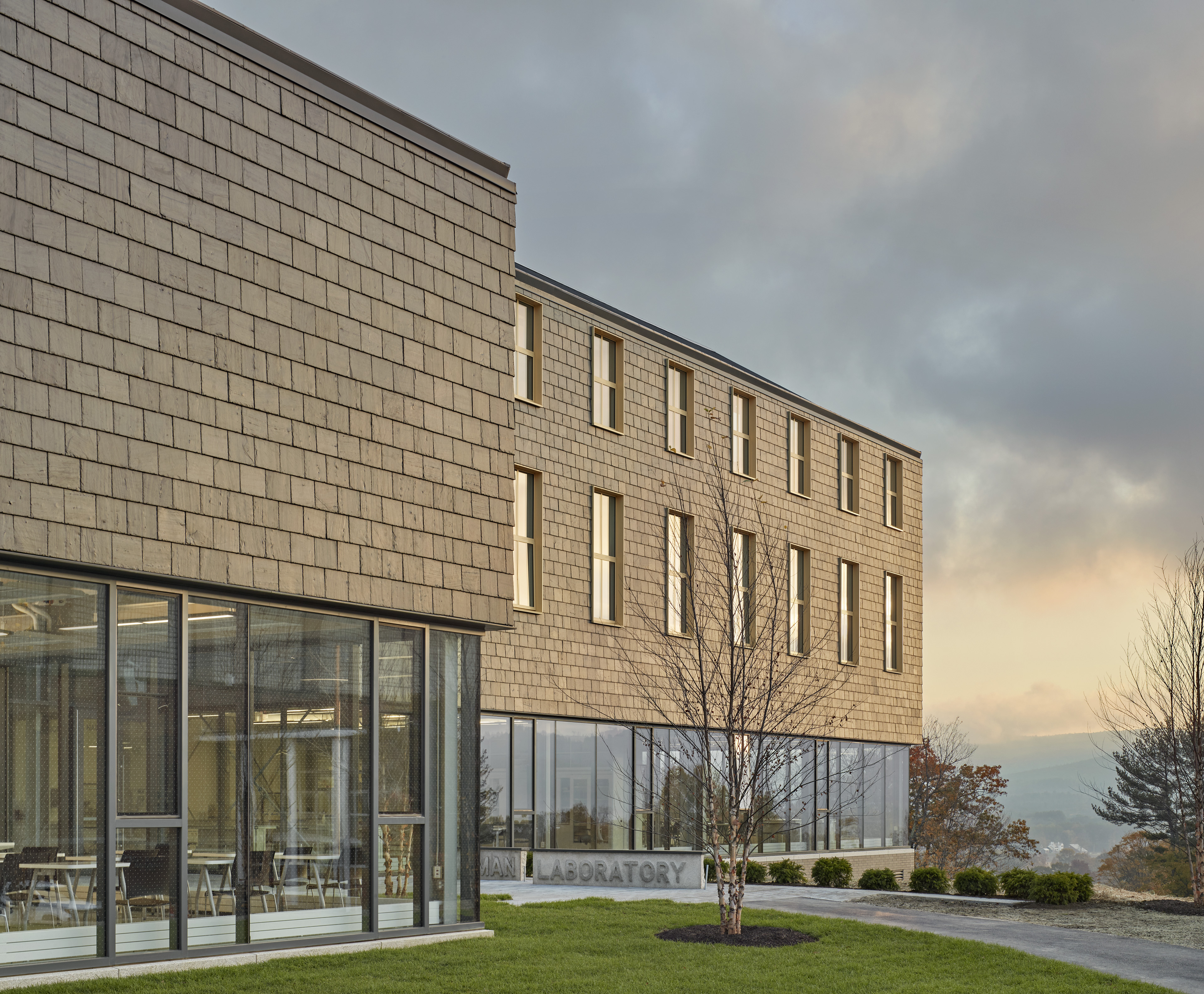 Exterior of laboratory with sun reflecting off side tiles. First floor with tall glass panels with sunset clouds behind