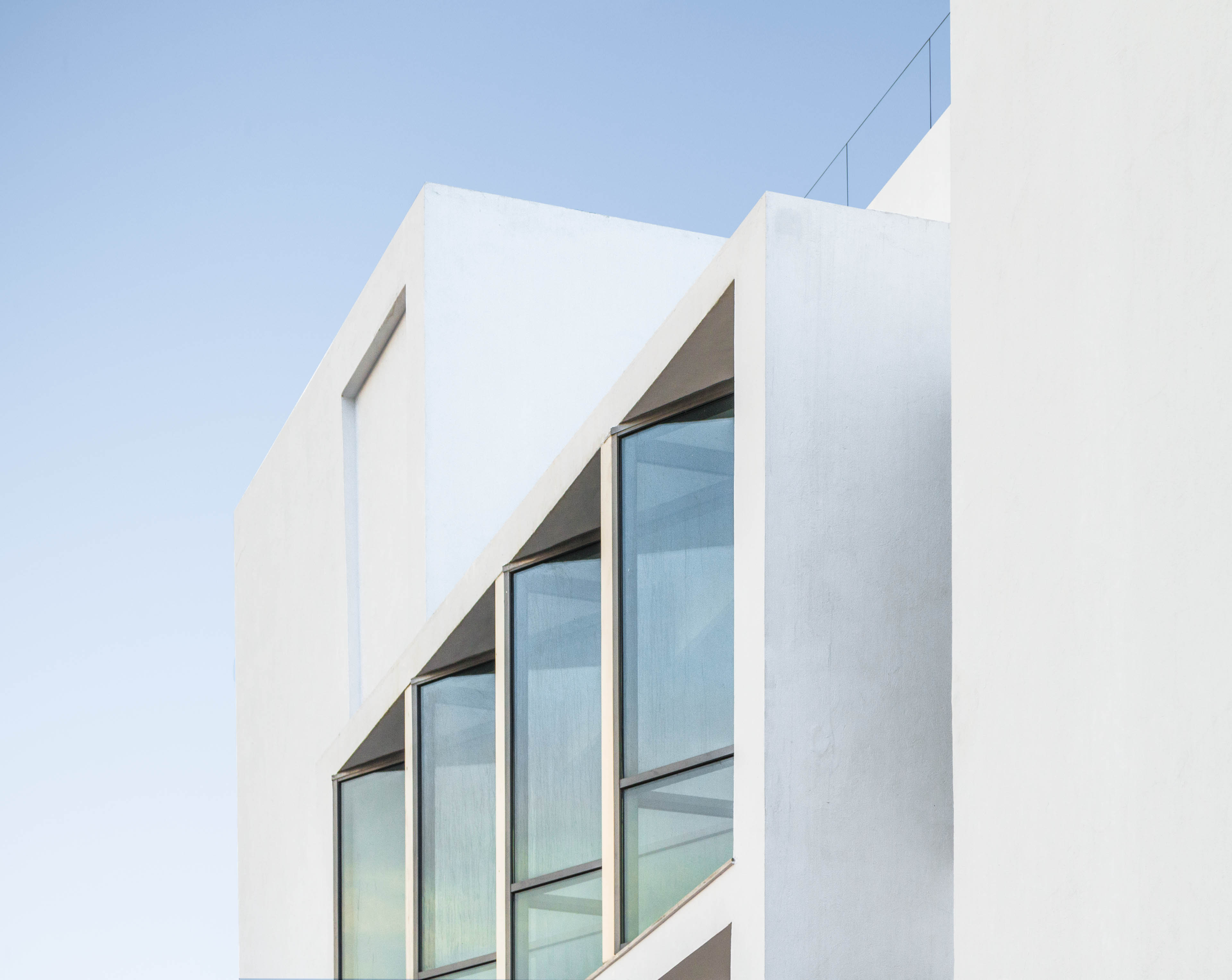 Portion of top left of building with long vertical windows and white facade. Blue sky in background