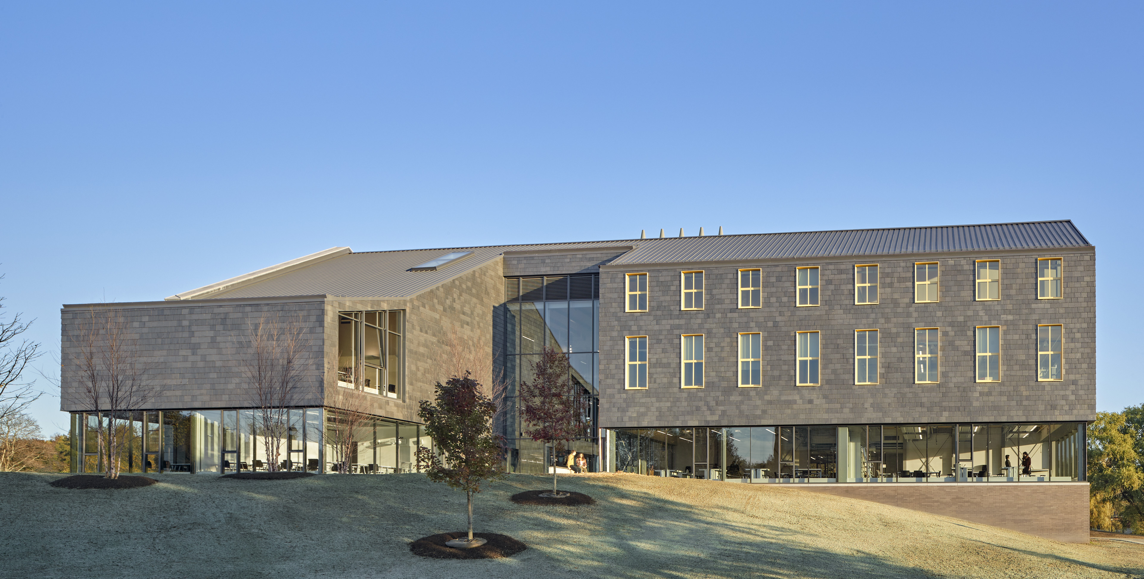 Exterior with slopped side on the left and to the right 2 floors with vertical windows with glass paneling inbetween both sides. Light blue sky with shadow over building
