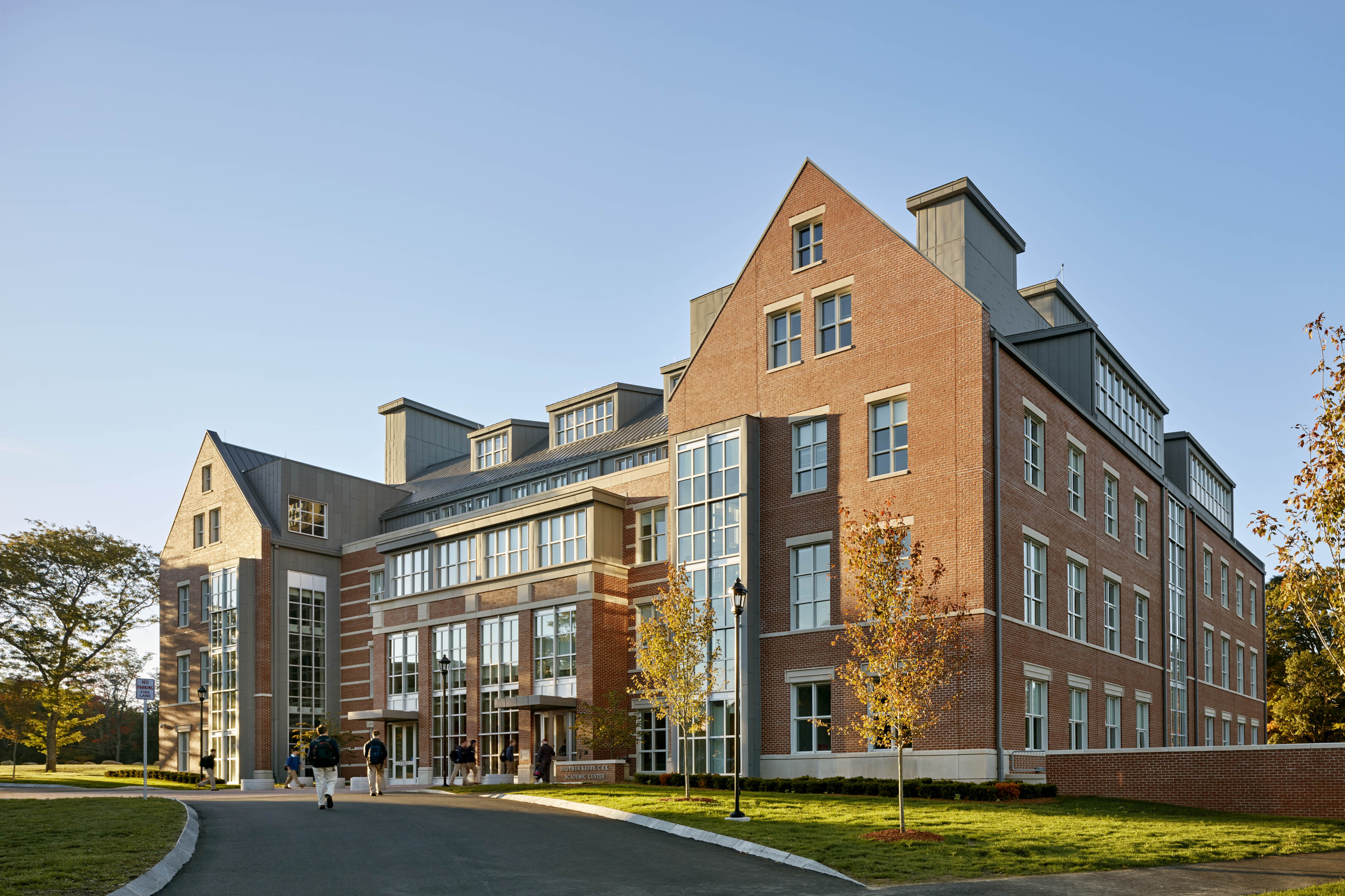 View of exterior from drop off lane, with students walking into building and sun shining 
