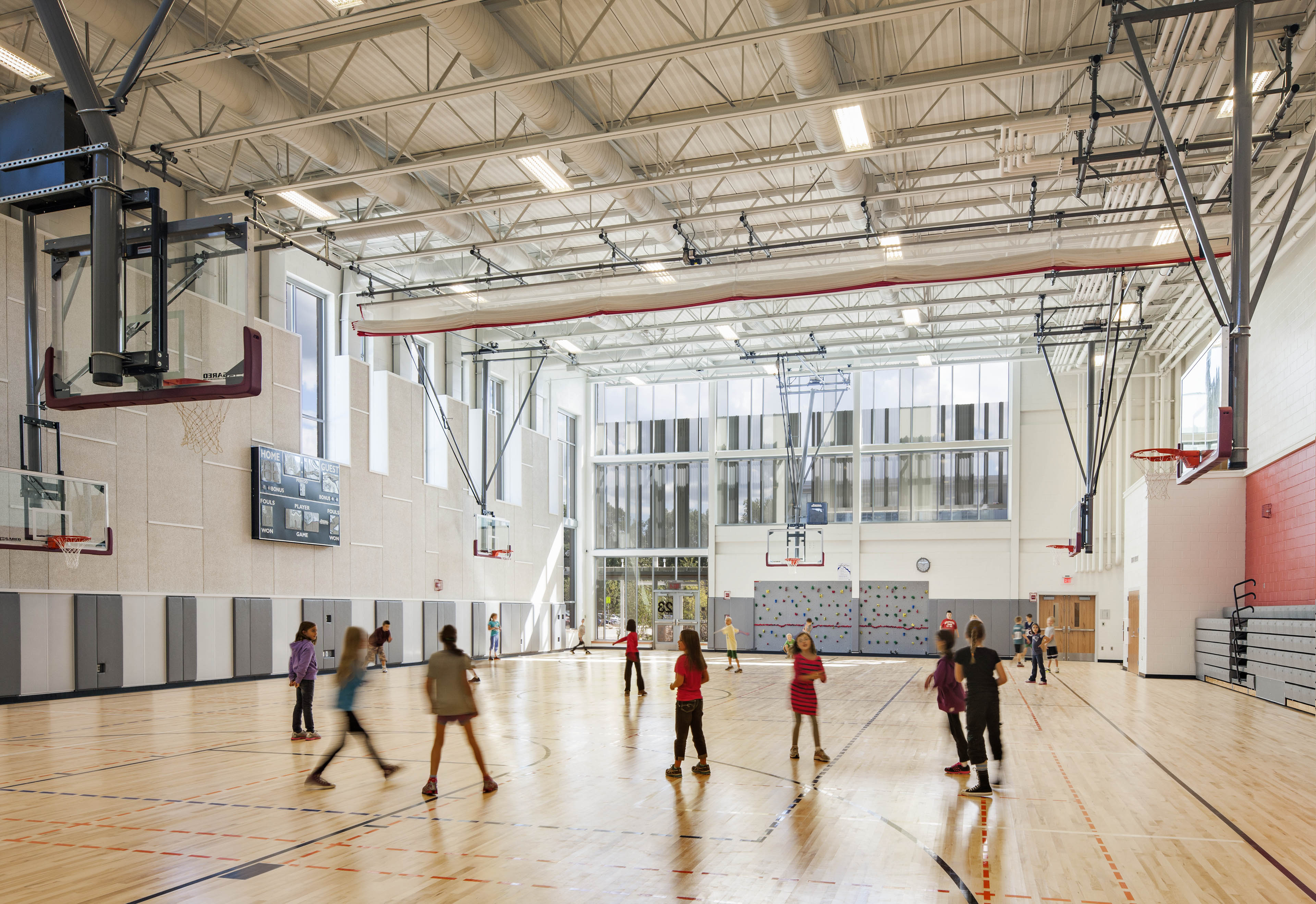 Students playing in gymnasium with basketball hoops on the left 
