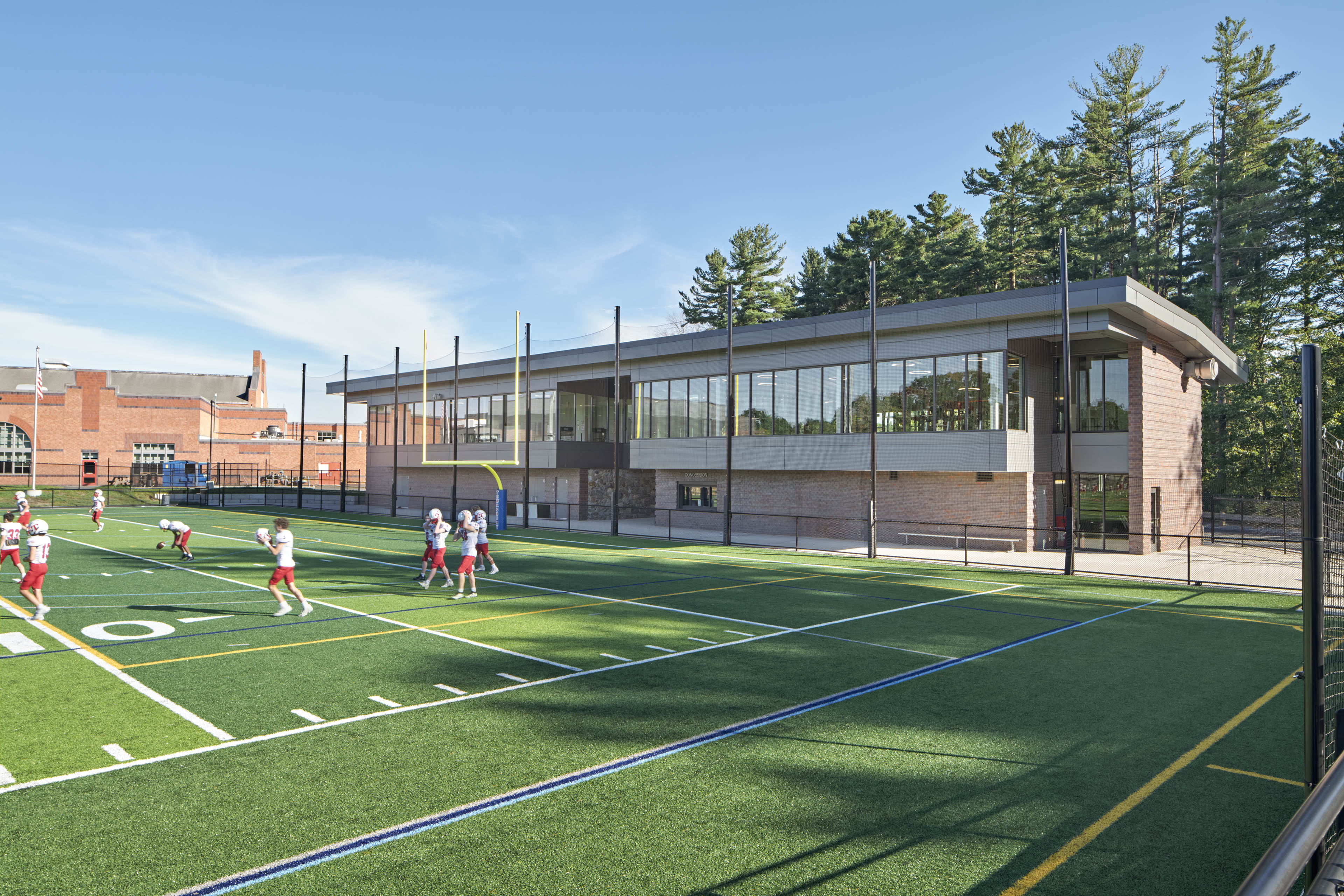 Football players using football field with trees behind building and blue sky above