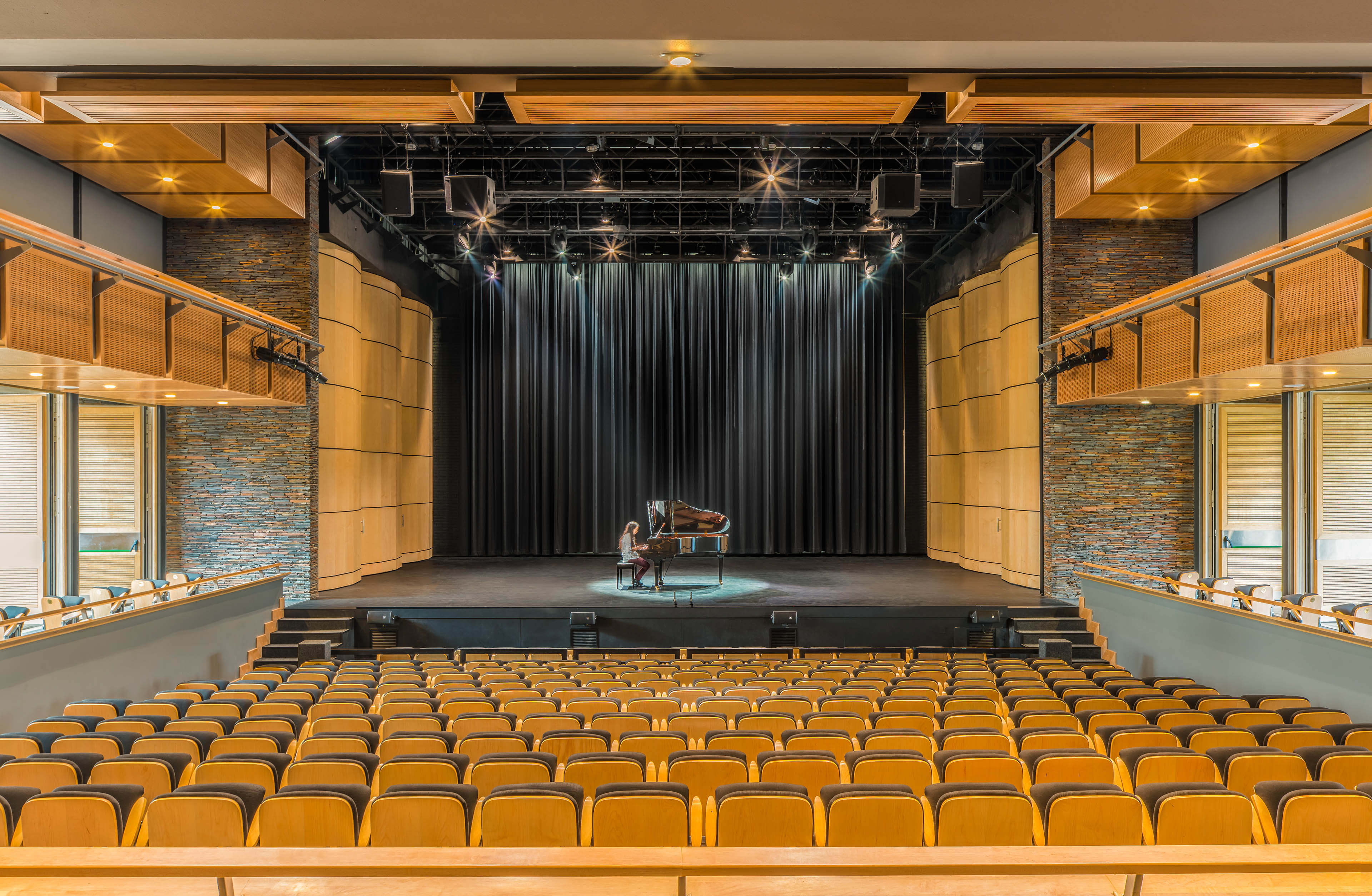 View from balcony of theater, with student playing grand piano with spotlight at center stage