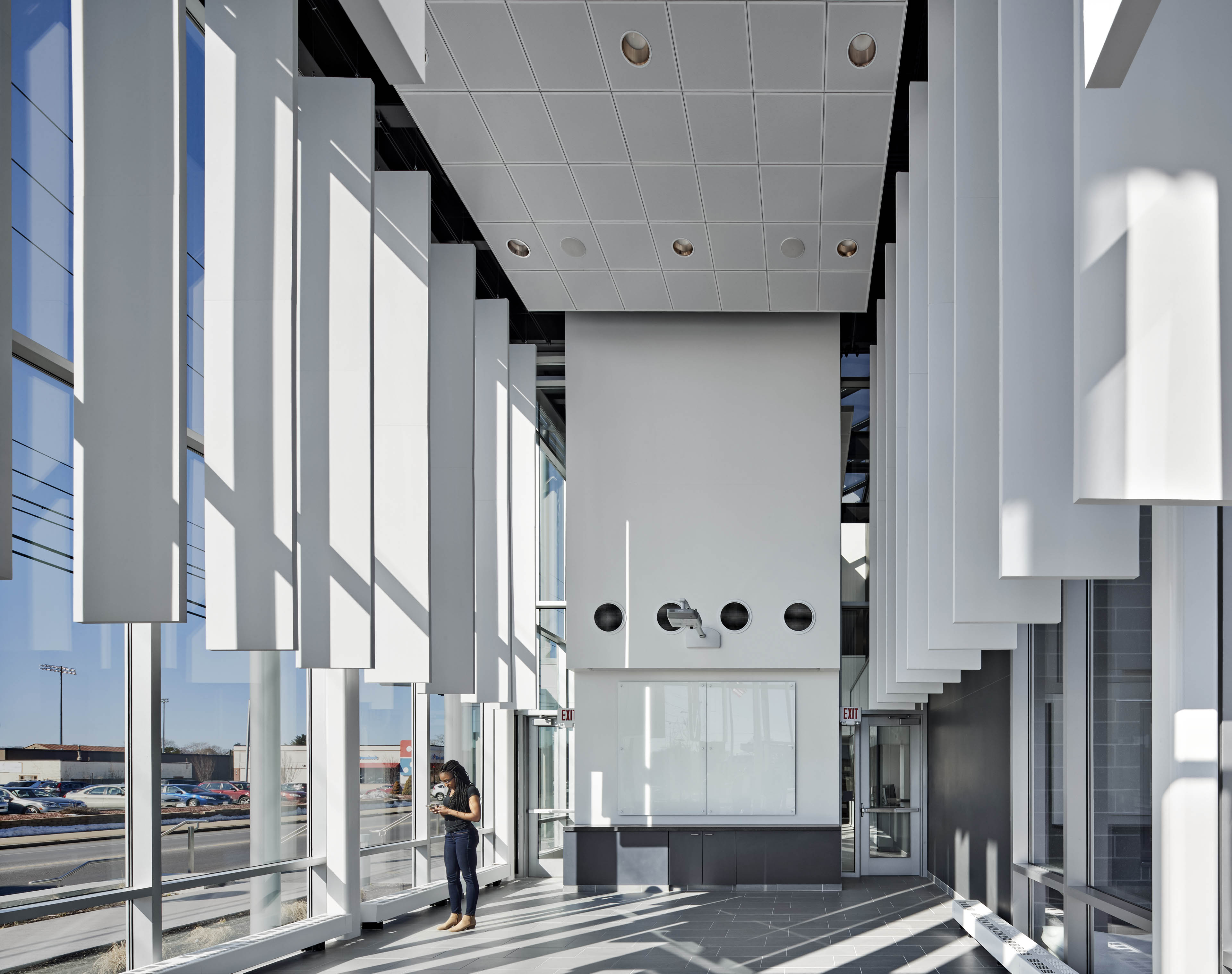 Patrons standing in lobby, left side of building has floor to ceiling windows with white panels hanging down