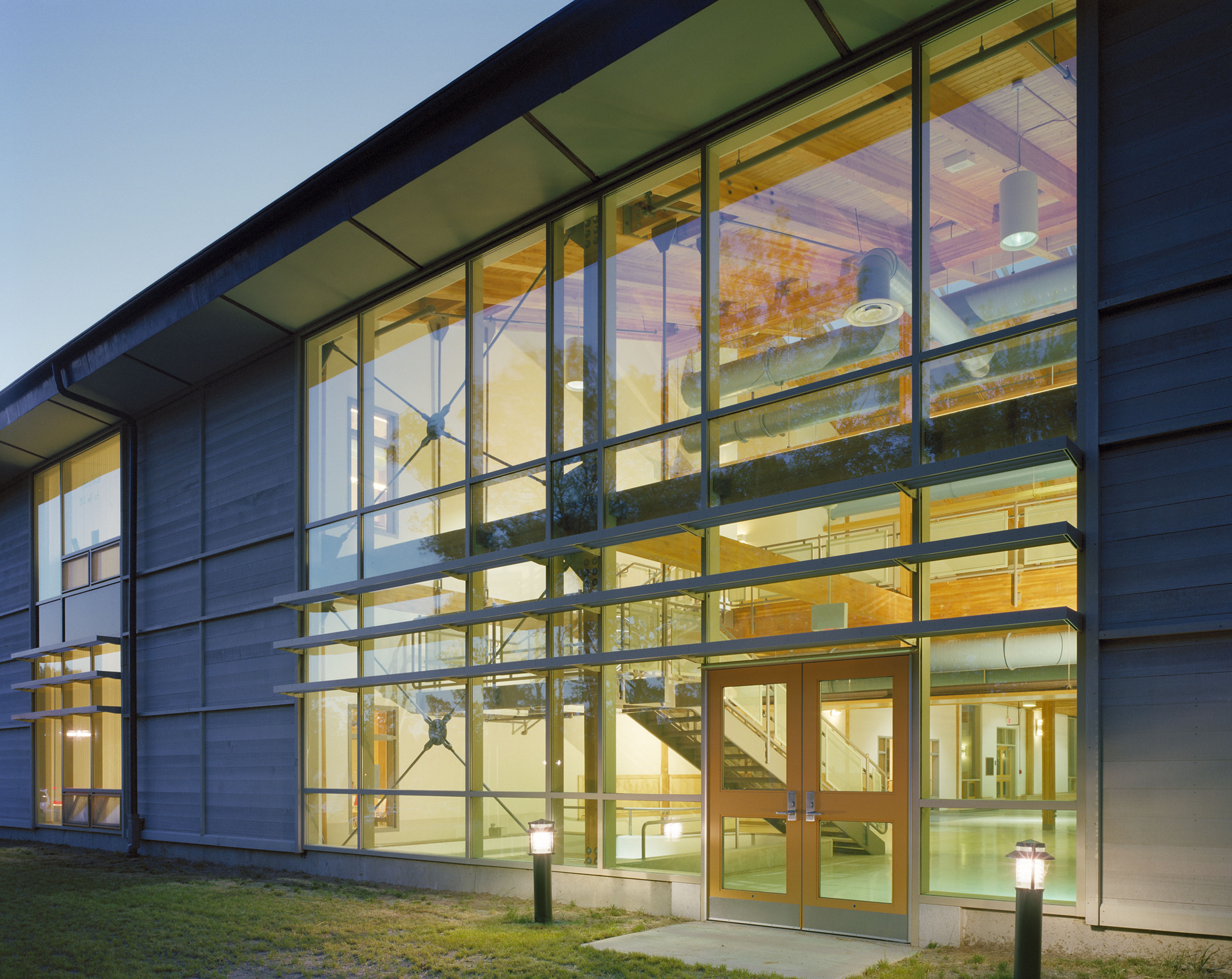 Front entrance of building with floor to ceiling windows at dusk with soft yellow light emitting
